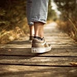 Person wearing sneakers walking on a wooden path in a sunlit park.